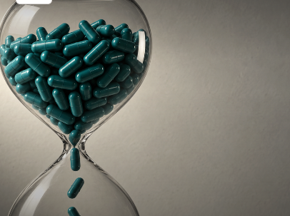 Glass hourglass filled with teal capsules streaming through its neck