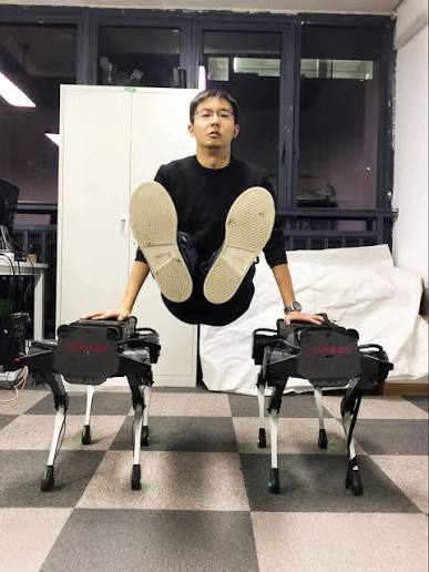 Wang Xingxing balancing between two early Unitree quadruped robots